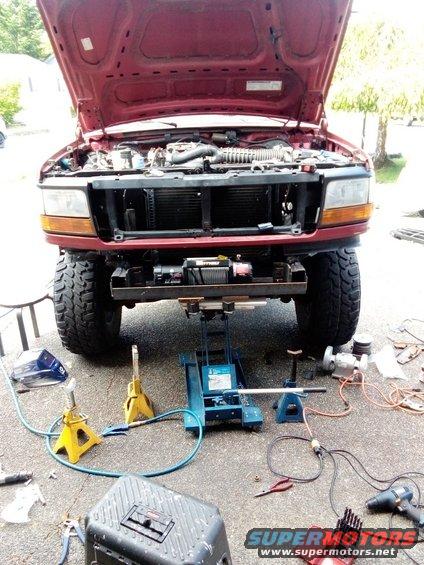 Red Ford truck with hood open, front view, jacked up, with winch installed on custom bumper