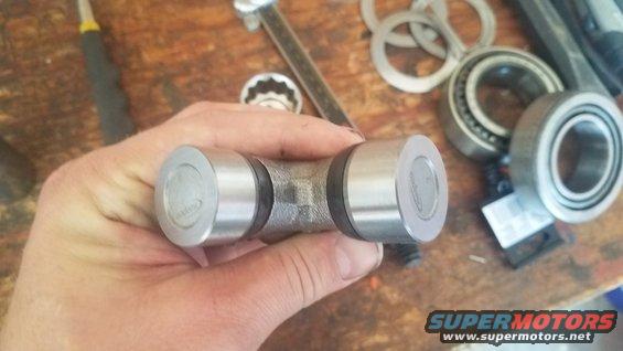 Hand holding a universal joint with bearings and tools in the background