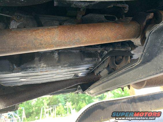 Underside of a vehicle showing rusted exhaust pipes and a transmission pan