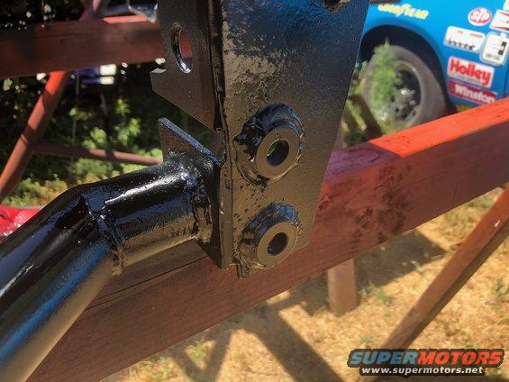 Black painted metal bracket with bolts, attached to red wooden beams. A blue race car is visible in the background