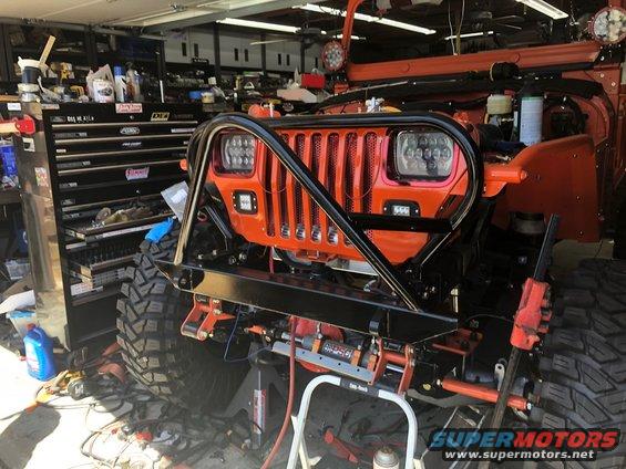 Orange Jeep Wrangler in garage, front view, with custom bumper and winch. Tool chest in background