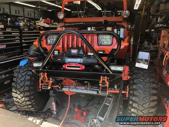 Orange Jeep Wrangler with winch, custom bumper, and large off-road tires, parked in a garage