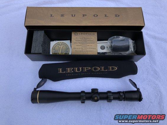 Black Leupold rifle scope with gold accents, in its box with accessories and a protective cover