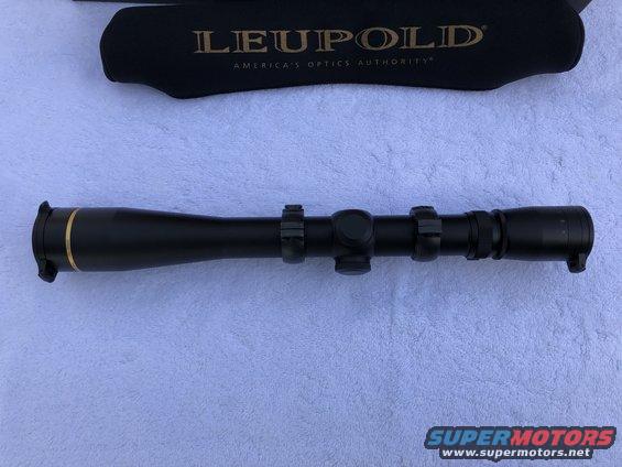 Black Leupold rifle scope with gold accents, mounted on rings, with a black lens cover behind it