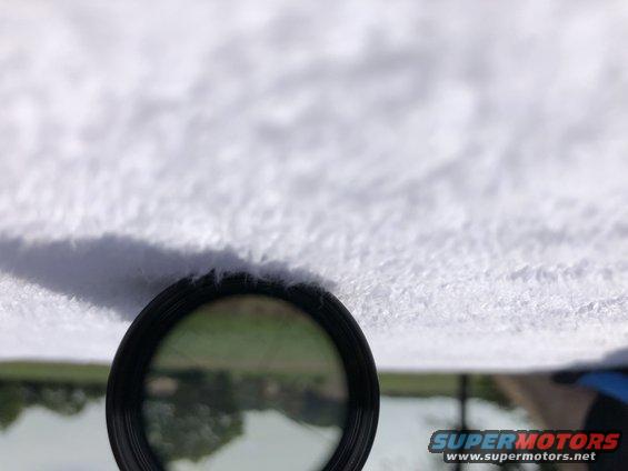 Close-up of a car's headliner with a magnifying glass showing a reflection of trees and water