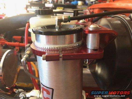 Close-up of an aftermarket aluminum fluid reservoir with red mounting bracket in an engine bay