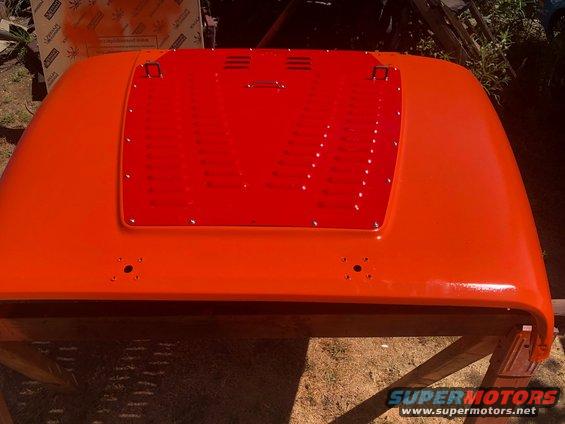 Orange Jeep Wrangler hood with red vent insert, resting on wooden supports