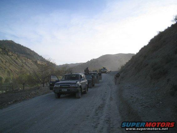 Dark Toyota Land Cruiser with open driver door on a dirt road, mountains in background