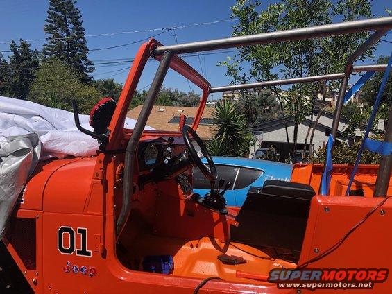 Orange Jeep interior with roll cage, "01" decal, and "Jeep" script. A blue car is visible behind it