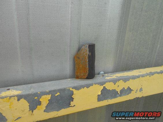 rusted metal wedge on a peeling yellow painted beam against a gray corrugated wall