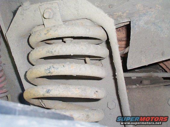Close-up of a dusty suspension coil spring with metal bracket and bolt