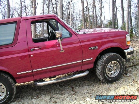 Red 1994 Ford Bronco parked on a dirt path with trees in the background