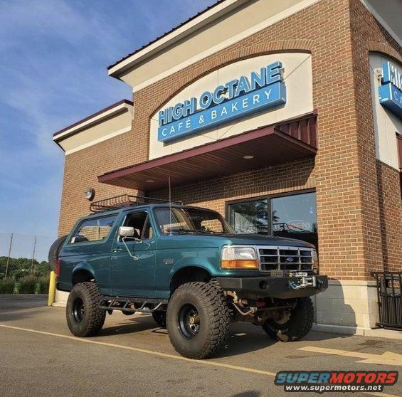 Teal SUV with lifted suspension and aftermarket wheels parked in front of a brick building with a blue sign