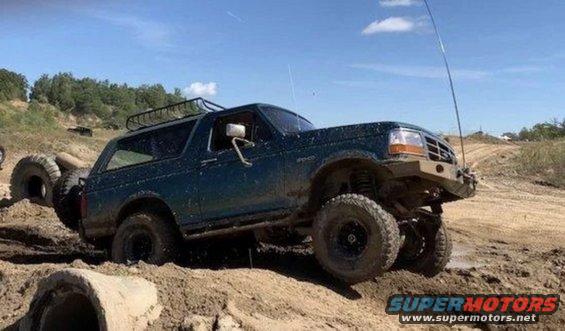1996 Ford Bronco navigating a muddy off-road course, with large tires and a roof rack