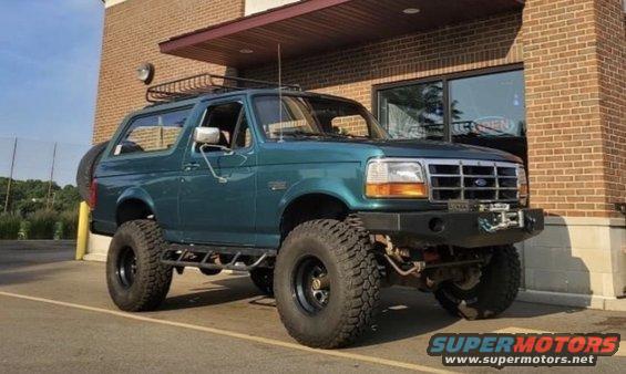 Green 1996 Ford Bronco with roof rack and off-road tires parked outside a brick building