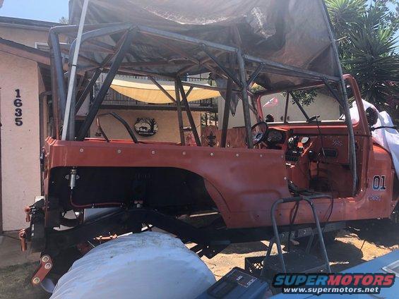 Orange Jeep CJ-7 body undergoing modification with a custom roll cage and tarp overhead. Number '01' is visible on the side