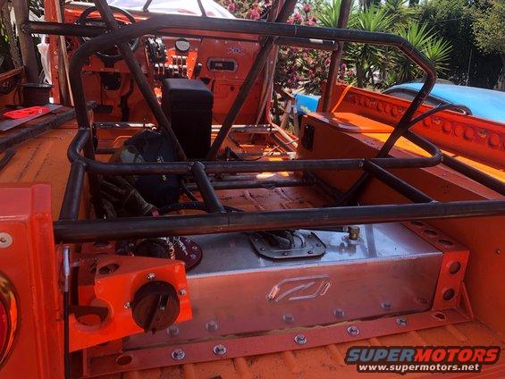 Off-road vehicle interior showing a roll cage, custom fuel tank, and orange interior panels. A Supermotors.net logo is visible
