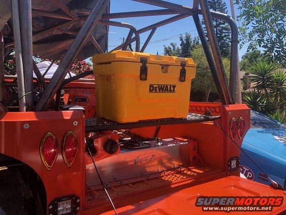 Yellow DeWalt cooler on a shelf above a metal fuel tank in an orange vehicle bed with a roll cage. Another vehicle is visible to the right