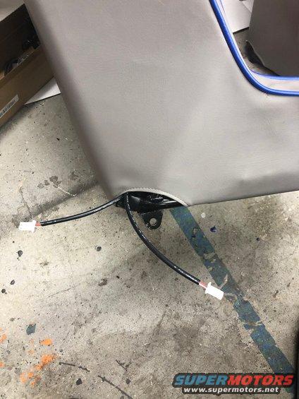 Gray car seat with blue piping and exposed wiring, showing a metal bracket and connectors