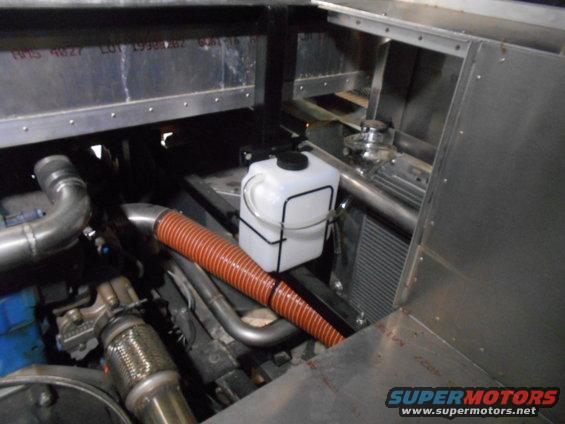 Engine bay with white coolant reservoir and orange hose