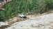 1995 Ford Bronco - A white pickup truck navigates a challenging off-road trail surrounded by dense forest and large rocks.