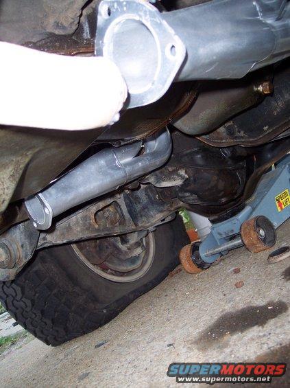 Underside of a vehicle with exhaust headers, a flat tire, and a jack