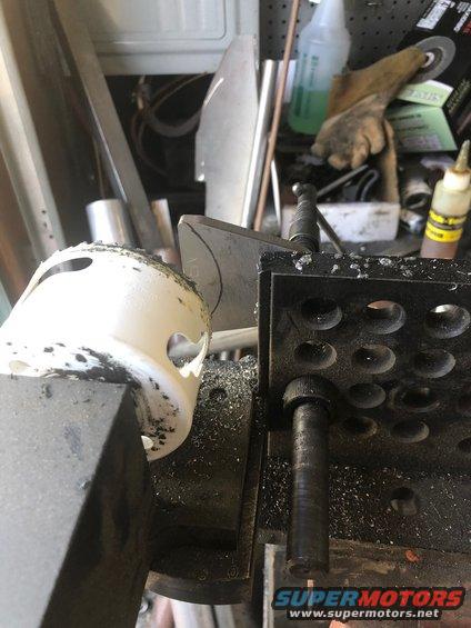 White plastic part with holes being machined in a vise with metal shavings
