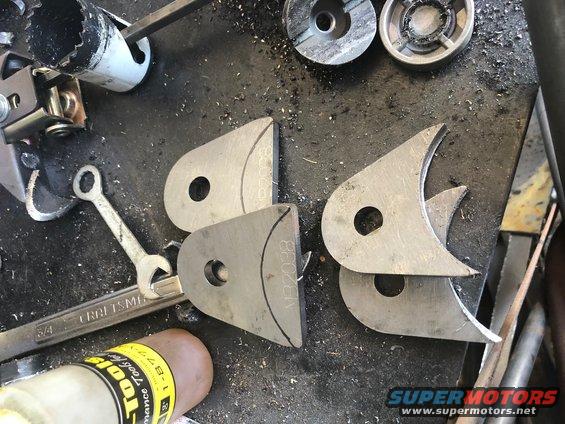 Metal tabs with holes and markings, a wrench, and a hole saw on a workbench