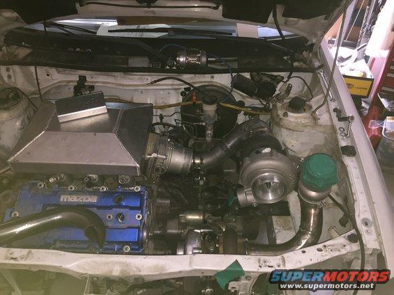 Engine bay with twin turbochargers, custom intake, and blue Mazda valve cover