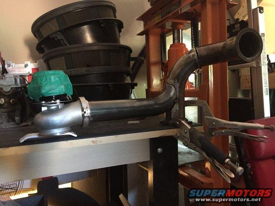 Turbocharger with green cover and bent exhaust pipe clamped to a workbench