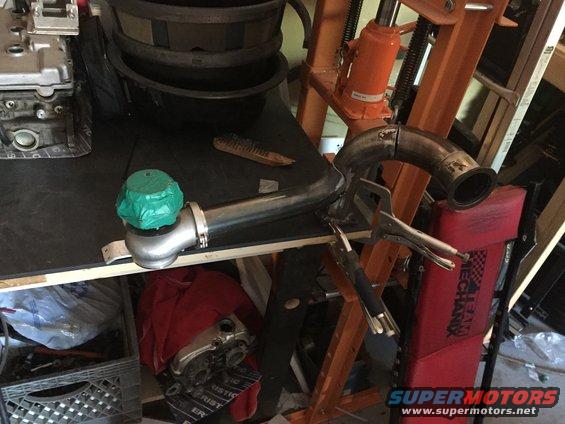 Turbocharger with green protective cover and exhaust pipe clamped to a workbench