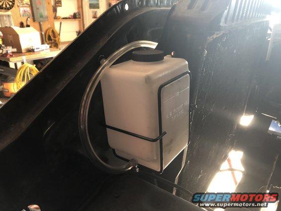 Windshield washer fluid reservoir mounted in engine bay, with tubing connected