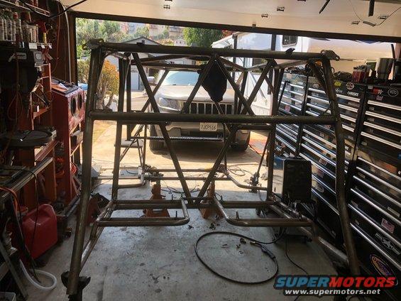 Metal roll cage structure in a garage with a Jeep Grand Cherokee visible in the background