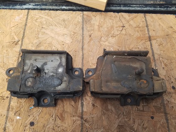 Two used motor mounts on a plywood surface