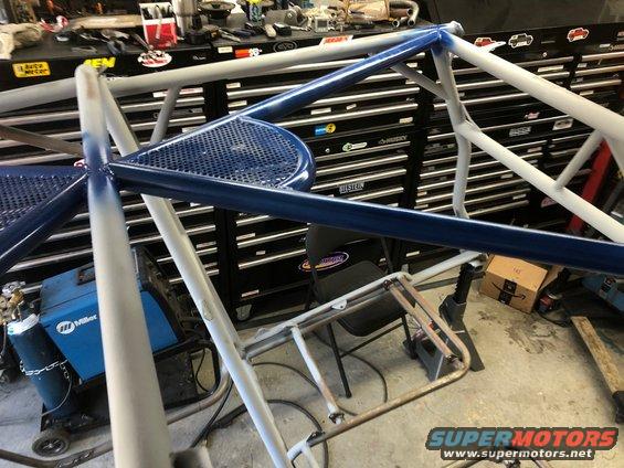 Roll cage frame with blue and gray paint, in a garage with toolboxes and a welder