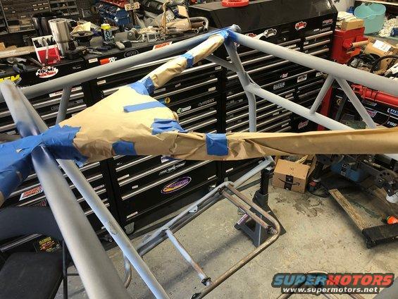 Roll cage tubing masked with brown paper and blue tape, in a workshop