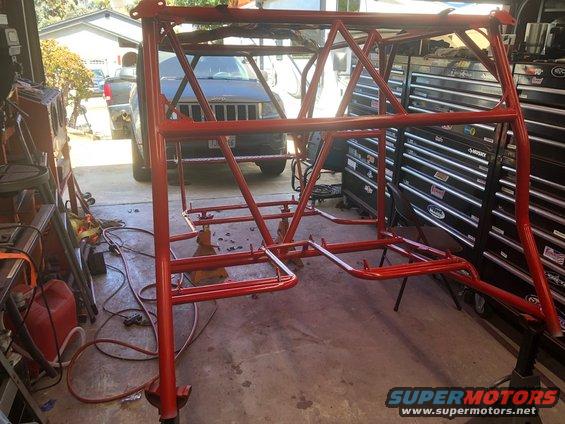 Red roll cage in garage, with a Jeep SUV in the background