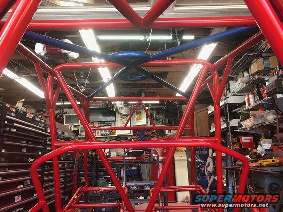 Red and blue roll cage structure in a workshop, with tool chests and shelves in the background