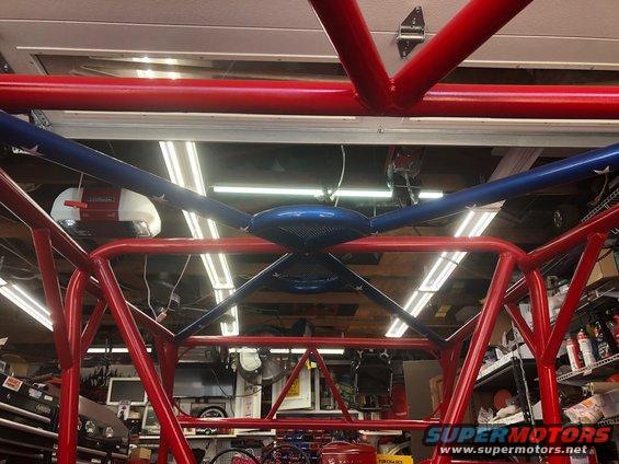 Red and blue metal roll cage tubes intersecting overhead in a garage setting