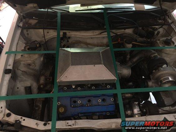 Engine bay with blue valve cover, custom intake box, and turbocharger. Green straps crisscross the engine compartment