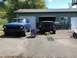 1978 Ford Bronco - A blue 1978 Ford Bronco sits in front of a garage next to a black truck undergoing repairs.