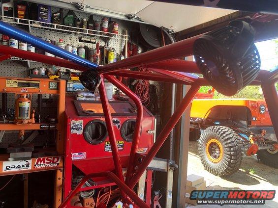 Red roll cage in foreground, orange Jeep with large tires in background
