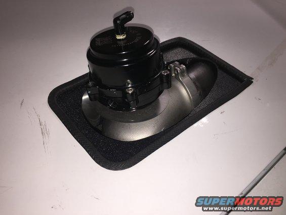 Black blow-off valve mounted on a silver pipe with a black rubber gasket on a white surface