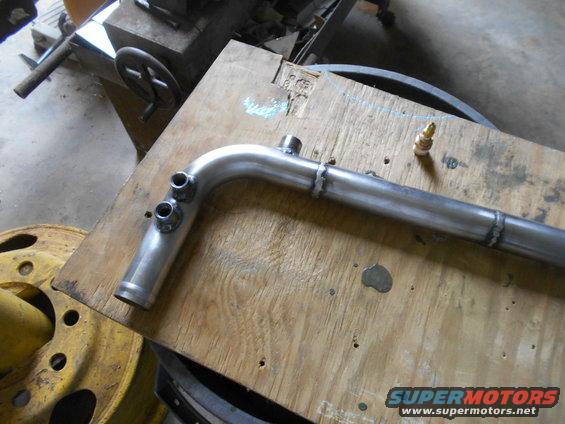 Custom metal pipe with multiple fittings on a wooden surface