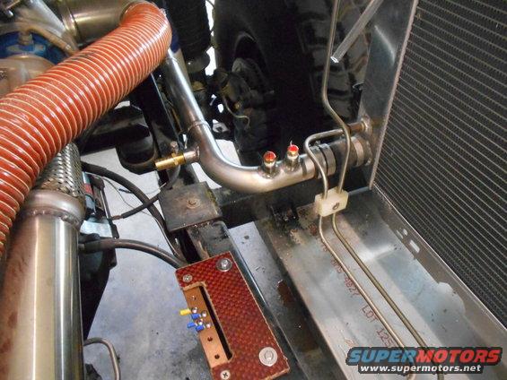 Engine bay with custom metal pipes, orange hose, and a radiator. Text on metal tray reads 'LOT 125'