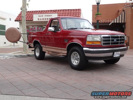 Red 1994 Ford Bronco parked in front of a barber shop, has a spare tire carrier on the back