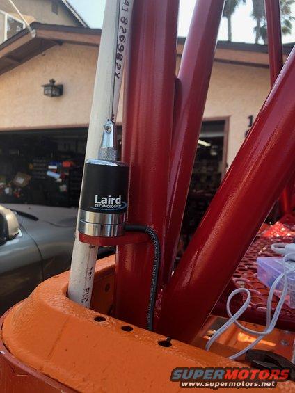 Orange and red roll cage with a black Laird Technologies antenna attached to a white pipe