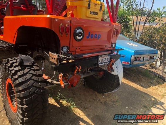 Orange 1992 Jeep Wrangler rear view with large off-road tires and a blue car behind it