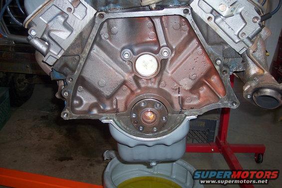 engine block, oil pan, and exhaust manifold on a stand. Oil is draining into a pan