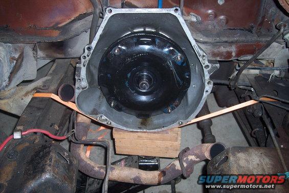Transmission bell housing with torque converter visible inside, supported by wood blocks and straps